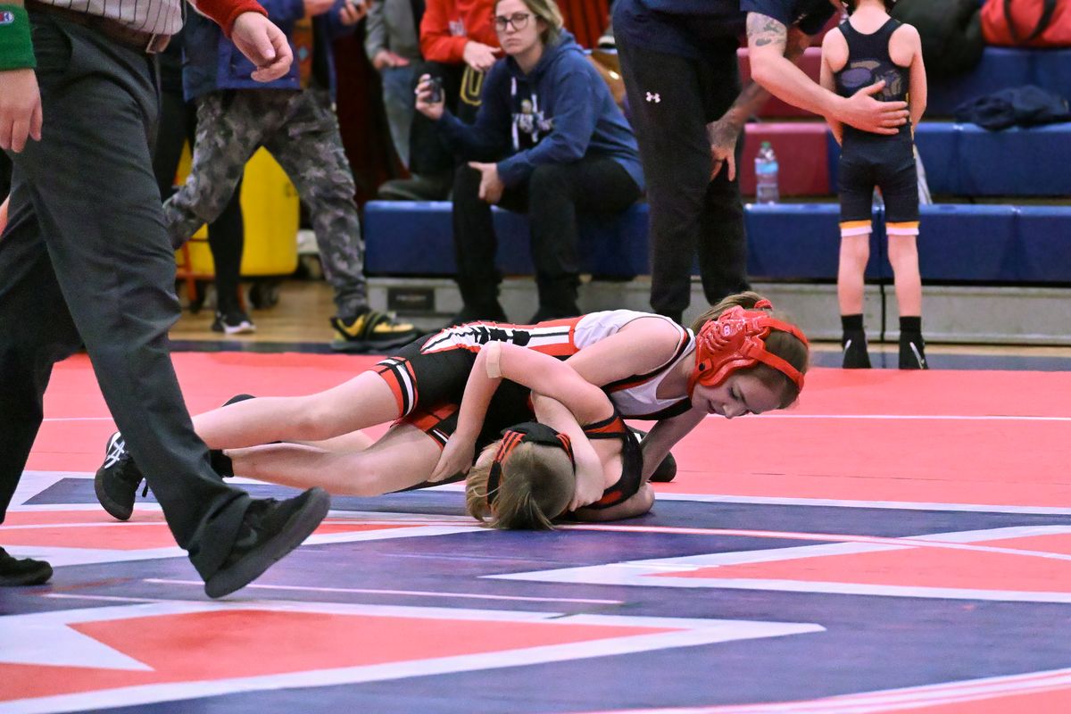 A young MSO girl wrestler in red headgear riding on top of her opponent.