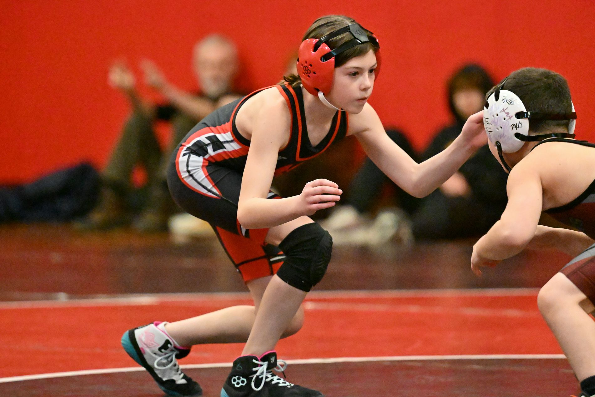 An MSO wrestler in red headgear, set in a low stance and locked in on an opponent.